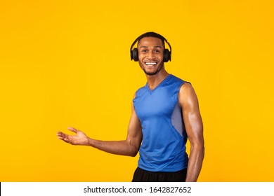 Young Black Sport Man Extending Hand With Open Palm To The Side As Inviting To Come Over Yellow Studio Wall, Copyspace