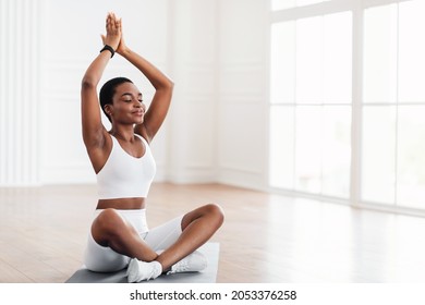 Young Black Sporty Woman Practicing Yoga, Doing Sukhasana Exercise, Easy Seat Pose Raising Arms Up Lifting Hands, Working Out Near Fitness Studio Window, Wearing White Pants And Top, Free Copy Space