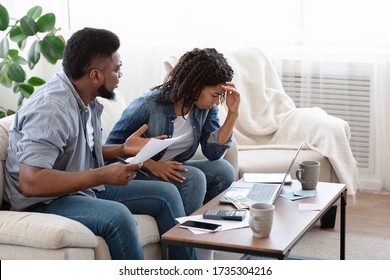 Young black spouses accounting family budget at home, husband scolding his wife for overspending and absence of money