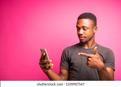 Young Black Stratified African Man Celebrating His Victory After Receiving Good News From His Mobile Phone. Man Standing On A Colorful Background Excited Pointing To His Mobile Phone 