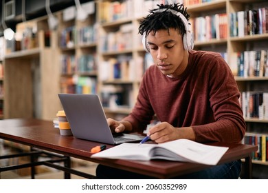 Young Black Student Reading While Using Laptop And Studying In A Library. 