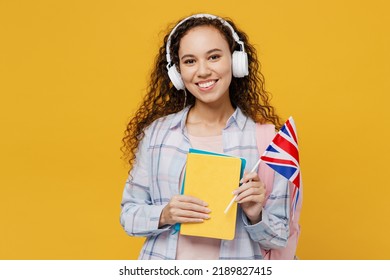 Young black teen girl student she wear casual clothes headphones backpack bag hold books british flag listen audiobook isolated on plain yellow color background High school university college concept - Shutterstock ID 2189827415