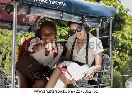 Young black tourist woman and white backpacker friend having fun on tuktuk local taxi during summer vacation in Chiang mai, Thailand