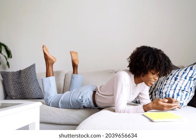 Young Black Woman With Afro Hair Laying Down On Couch Using Her Phone