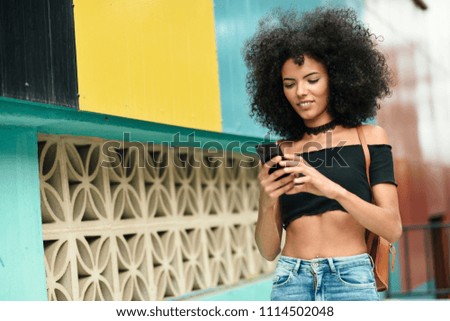 Frau mit Afro-Haaren auf der Straße, die ein Smartphone hält.