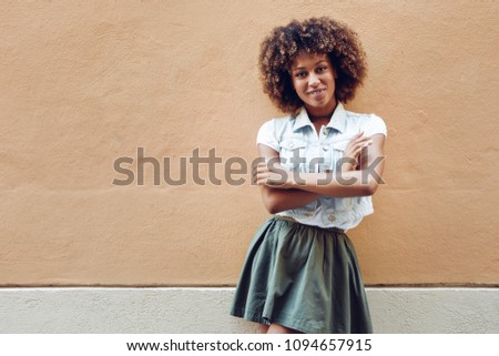 Young black woman, afro hairstyle, smiling near a wall in the street