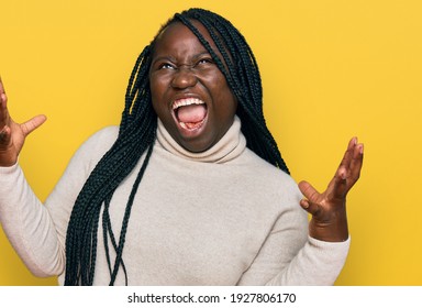 Young Black Woman With Braids Wearing Casual Winter Sweater Crazy And Mad Shouting And Yelling With Aggressive Expression And Arms Raised. Frustration Concept. 