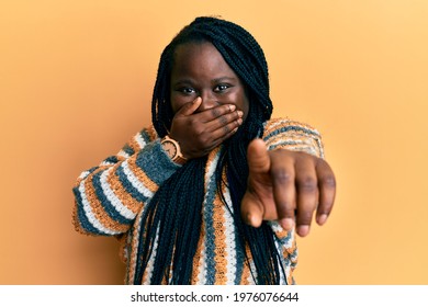 Young Black Woman With Braids Wearing Casual Winter Sweater Laughing At You, Pointing Finger To The Camera With Hand Over Mouth, Shame Expression 