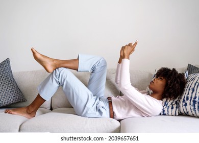 Young black woman with curly hair laying down on couch using her phone