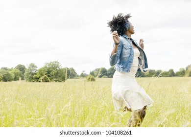 Young Black Woman Dancing In A Long Grass Field While Listening To Music With Her Headphones.