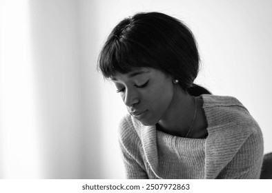 Young black woman in deep thought, captured in a serene black and white portrait. The image emphasizes emotional depth and introspection, highlighting her pensive expression. - Powered by Shutterstock