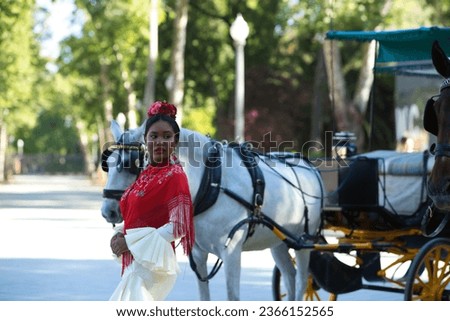 Young black woman dressed as a flamenco gypsy in a famous square in Seville, Spain. She is wearing a beige dress with ruffles and a red shawl and is standing next to a horse-drawn carriage