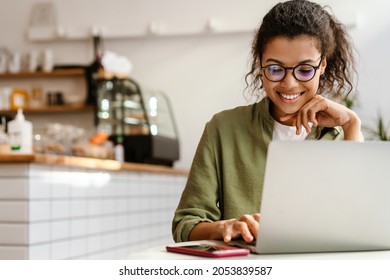 Young black woman in eyeglasses working with laptop while sitting at cafe indoors - Shutterstock ID 2053839587