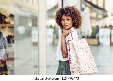 Young black woman in front of a shop window in a shopping street. African girl with afro hairstyle wearing casual clothes.