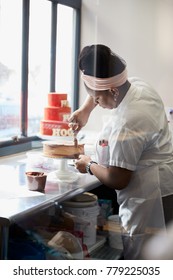 Young Black Woman Frosting A Cake At A Bakery