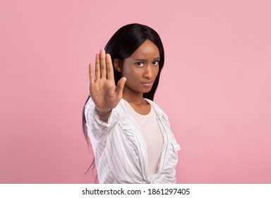 Young black woman gesturing STOP on pink studio background. Displeased African American lady saying NO, showing rejection gesture, expressing her negative attitude