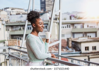 A young black woman is having coffee on the balcony. African American woman drinking coffee in sun sitting outdoor in sunshine light enjoying her morning coffee. - Powered by Shutterstock