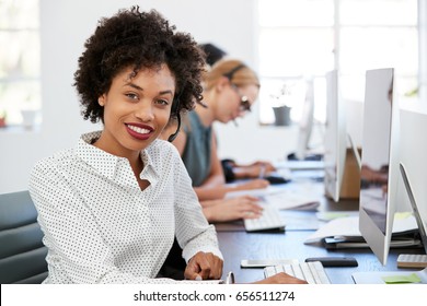 Young black woman with headset smiling to camera in office