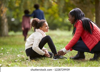 Young black woman helping her daughter to tie her shoes during a family walk in the park, low angle