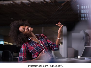 young black woman at her workplace in startup business office listening music on headphones and playing music instruments while relaxing - Powered by Shutterstock