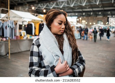 Young Black Woman Looking Goods In A Street Market In London. She Is Wearing A Coat And Scarf.