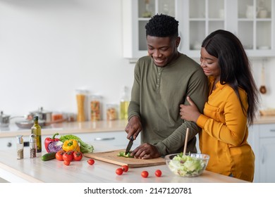 Young Black Woman Looking At Her Husband Cooking Salad In Kitchen, Happy Millennial African American Couple Preparing Healthy Food At Home Together, Enjoying Domestic Leisure, Copy Space - Powered by Shutterstock