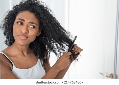 Young black woman looking her curly hair at mirror - Powered by Shutterstock