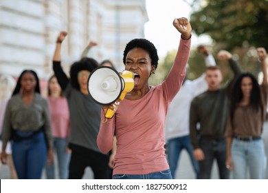 Young black woman with megaphone leading a group of demonstrators on the street. International group of people protesting for human rights and against racism, yelling slogans and raising fists up