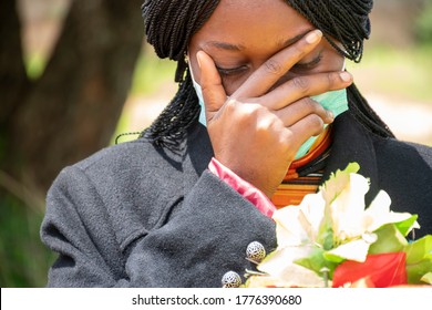 A Young Black Woman Mourning, Wearing Black And Holding Flowers