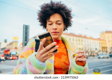 Young black woman outdoor using smartphone texting or watching video live streaming online