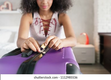 Young Black Woman Packing And Locking Bag For Holidays. Latino Girl Preparing Padlock For Travel Suitcase. Close-up Of Hands And Lock