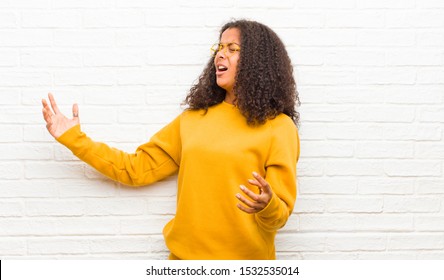 Young Black Woman Performing Opera Or Singing At A Concert Or Show, Feeling Romantic, Artistic And Passionate Against Brick Wall