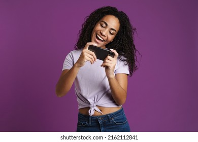 Young Black Woman Playing Online Game On Mobile Phone Isolated Over Purple Background