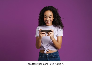 Young Black Woman Playing Online Game On Mobile Phone Isolated Over Purple Background