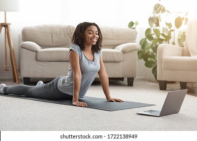 Young Black Woman Practicing Yoga At Home With Laptop, Watching Online Tutorials, Excersising In Living Room, Free Space