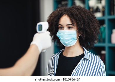 Young black woman in protective mask getting temperature check up in salon, close up - Powered by Shutterstock