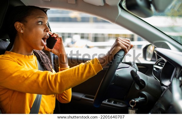 Young black woman shocked while talking on\
mobile phone and driving car\
outdoors