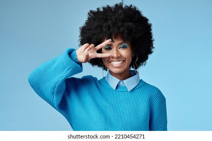 Young, black woman and shows peace sign with blue studio background, trendy style and afro. Smile, happy and relax African American female, lady or girl influencer with casual fashion and cosmetics. - Powered by Shutterstock