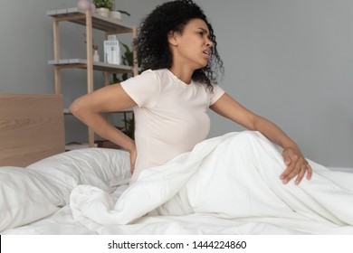 Young Black Woman Sit On Bed Touching Sore Back Feel Morning Backpain, Upset African Girl Suffer From Lower Lumbar Discomfort Muscle Pain Waking Up With Backache After Sleep On Uncomfortable Mattress