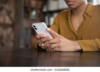 Young Black woman sitting at table, typing on smartphone, holding cellphone on wooden desk. Close up of hands. African American girl making call, browsing, chatting on social network, texting message