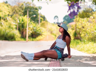 Young Black Woman Skater Sitting On Skateboard In The Street.