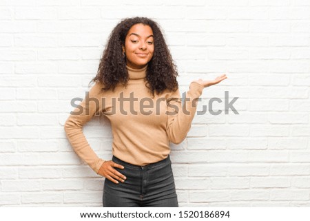 young black woman smiling, feeling confident, successful and happy, showing concept or idea on copy space on the side against brick wall