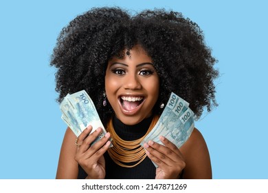 Young Black Woman Smiling Holding Brazilian Money Bills, Positively Surprised, Space For Text, Person, Advertising Concept, Isolated On Blue Background.