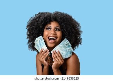 Young Black Woman Smiling Holding Brazilian Money Bills, Positively Surprised, Space For Text, Person, Advertising Concept, Isolated On Blue Background.