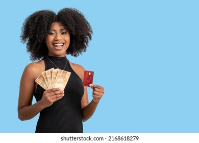 Young Black Woman Smiling Holding Brazilian Money Bills And A Chip Card, Positively Surprised, Space For Text, Person, Advertising Concept, Isolated On Blue Background