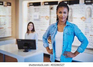 Young Black Woman Smiling Standing In Her Store With A Colleague In Backgorund