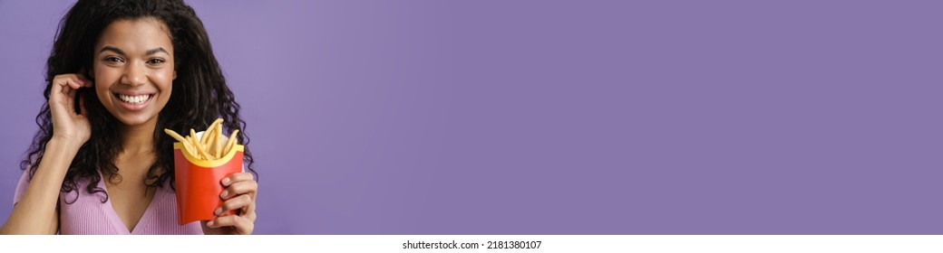 Young Black Woman Smiling While Eating French Fries Isolated Over Purple Background