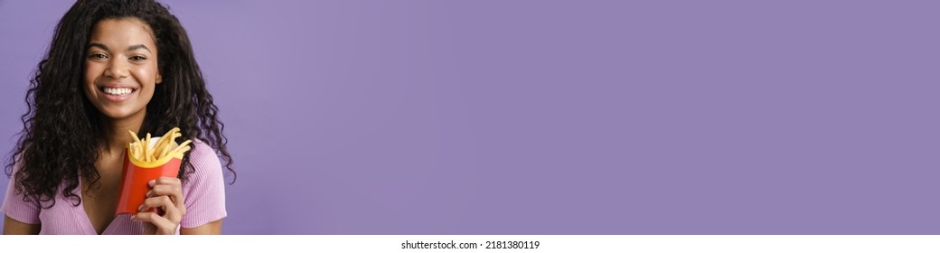 Young Black Woman Smiling While Eating French Fries Isolated Over Purple Background