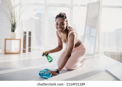 Young Black Woman In Sports Outfit Cleaning Yoga Mat After Workout At Home Gym, Free Space. Millennial African American Lady Using Detergent Spray, Disinfecting Equipment At Fitness Studio