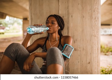 Young Black Woman In Sportswear Is Drinking Water From A Bottle While Sitting On Floor